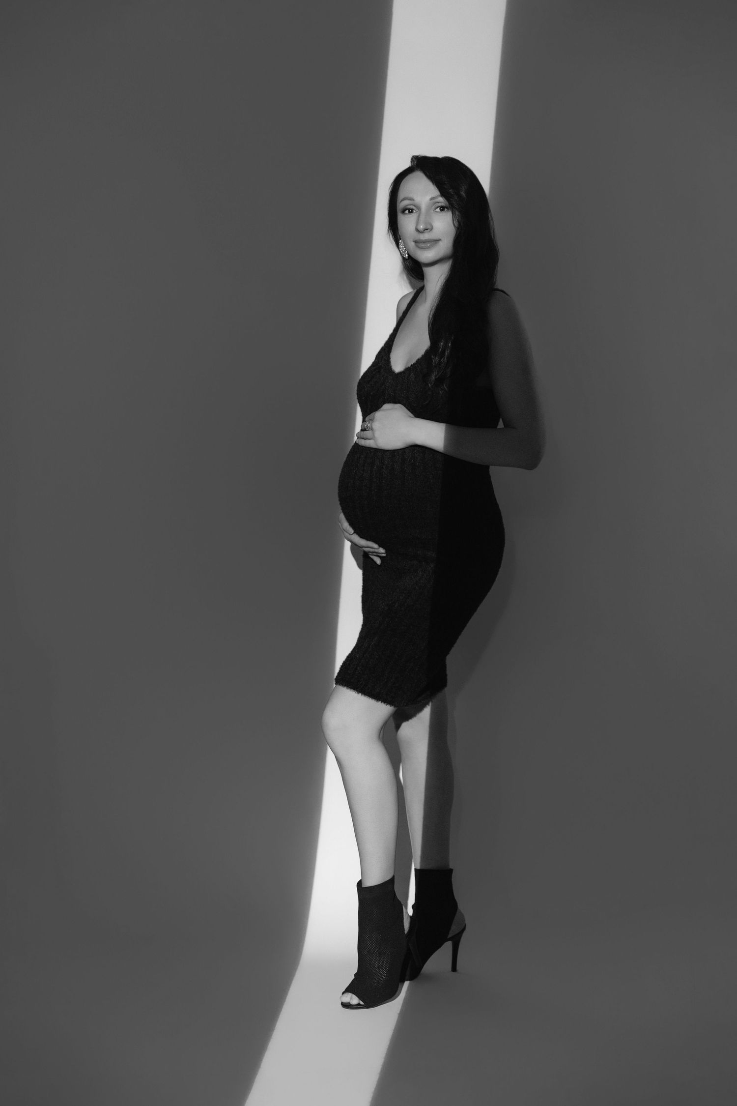 Artistic black and white maternity portrait against dramatic studio lighting.