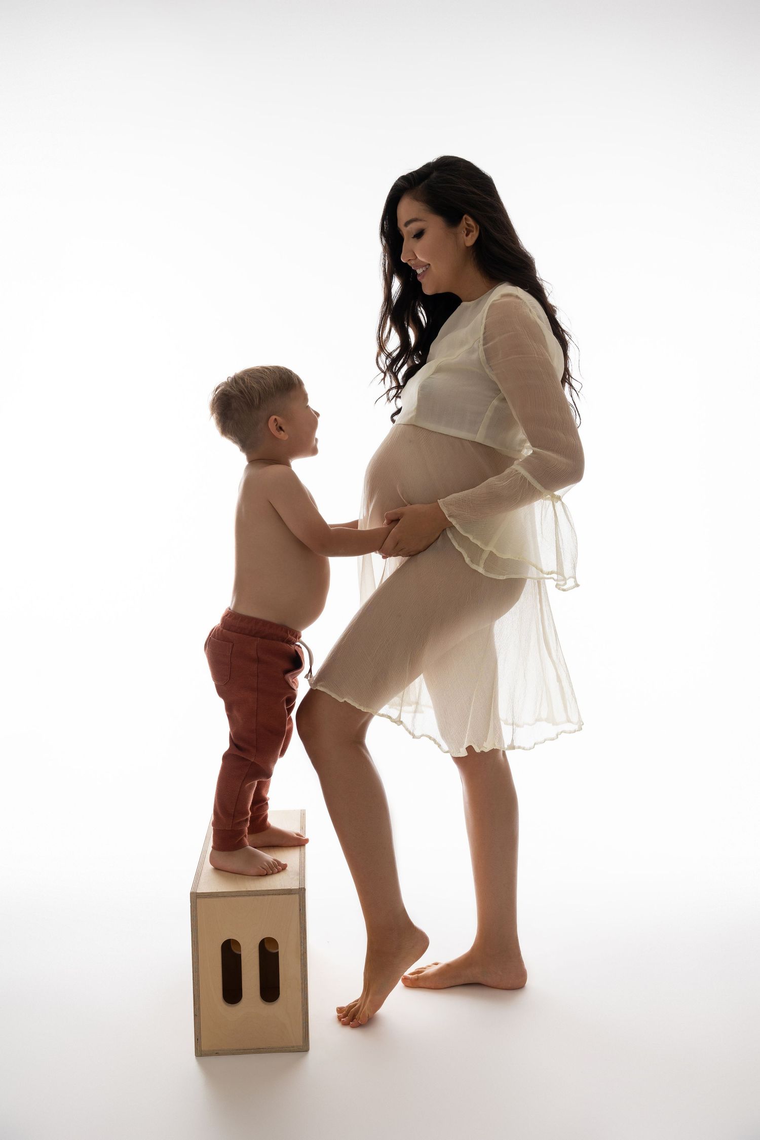 A series of photographs showing a toddler in red shorts interacting with pregnant figure near a wooden box against white background.