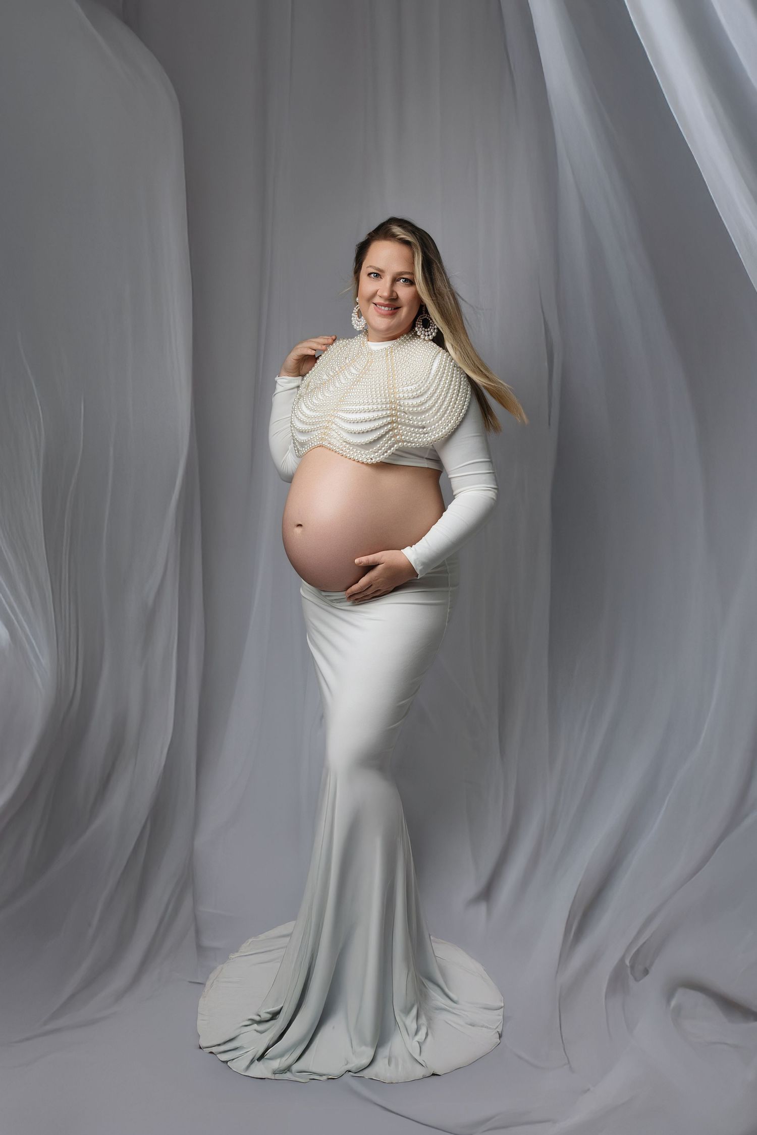 A maternity photoshoot series showing poses in a white fitted dress against a light gray backdrop.