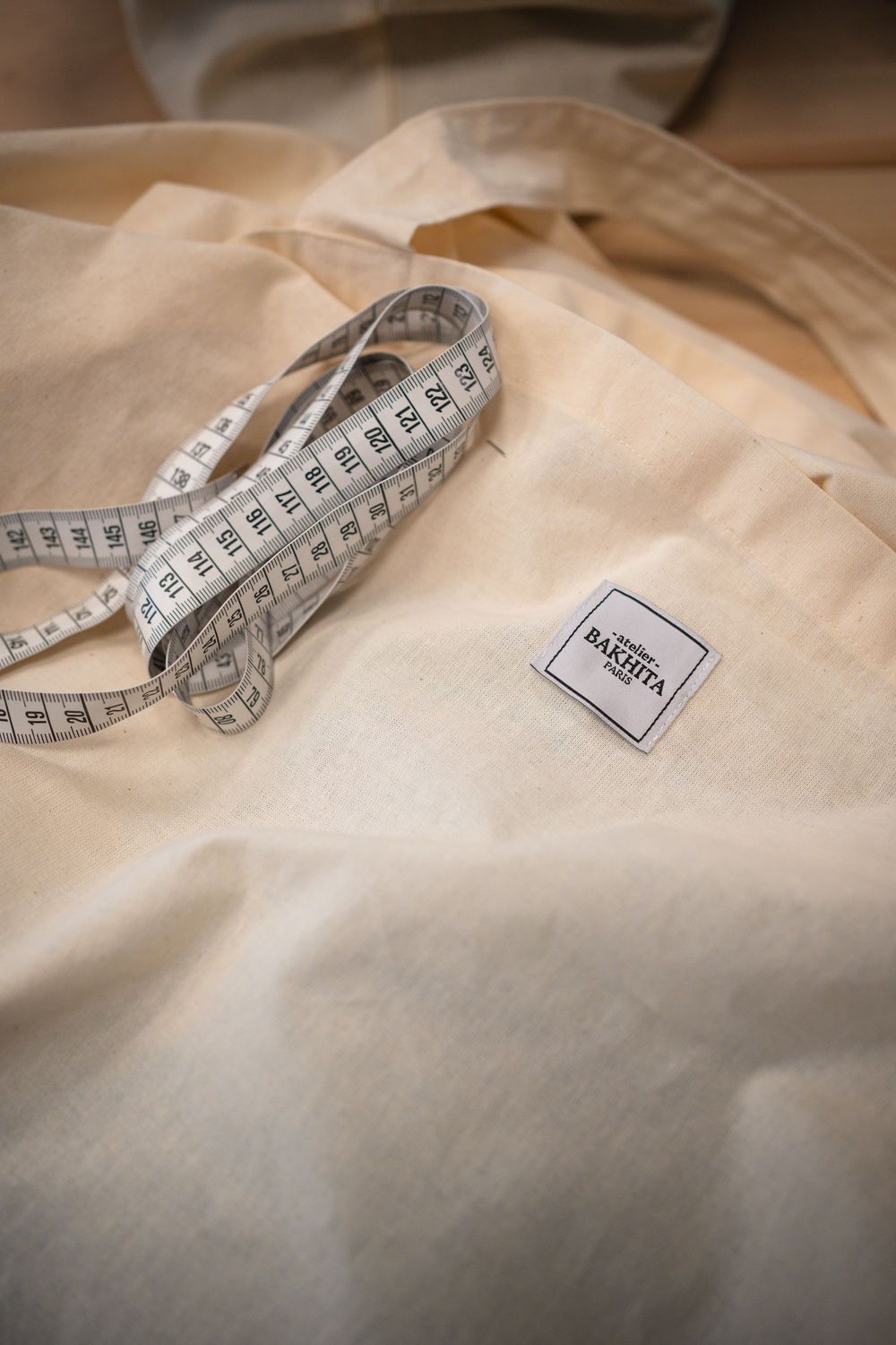 A white measuring tape lies curled on a light beige fabric surface showing tailoring and dressmaking details.
