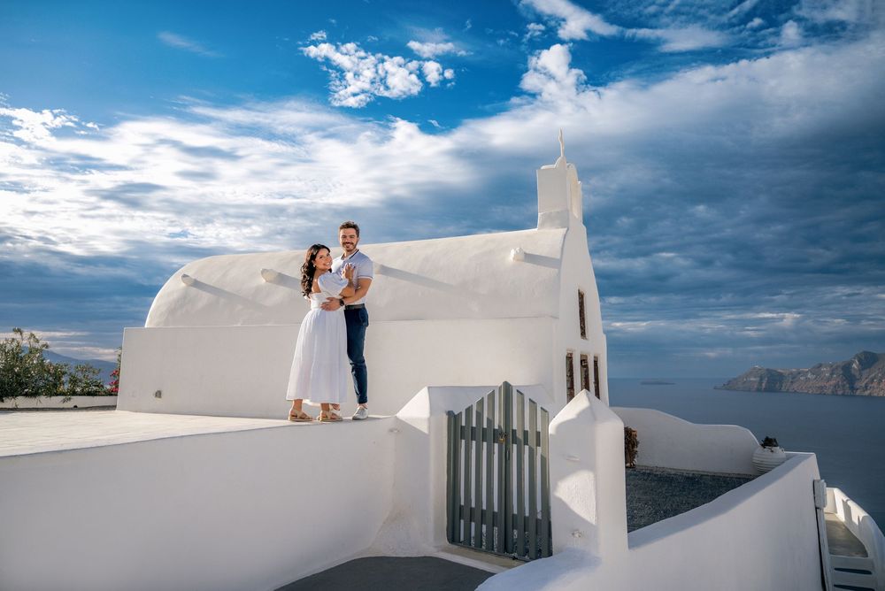 Couple enjoying a romantic moment on white-washed terraces overlooking the Mediterranean Sea in Santorini, Greece.