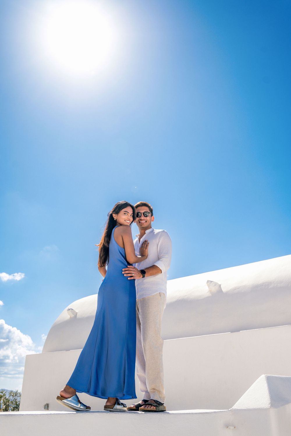 Romantic photoshoot on Santorini's white walls with bright blue sky backdrop.