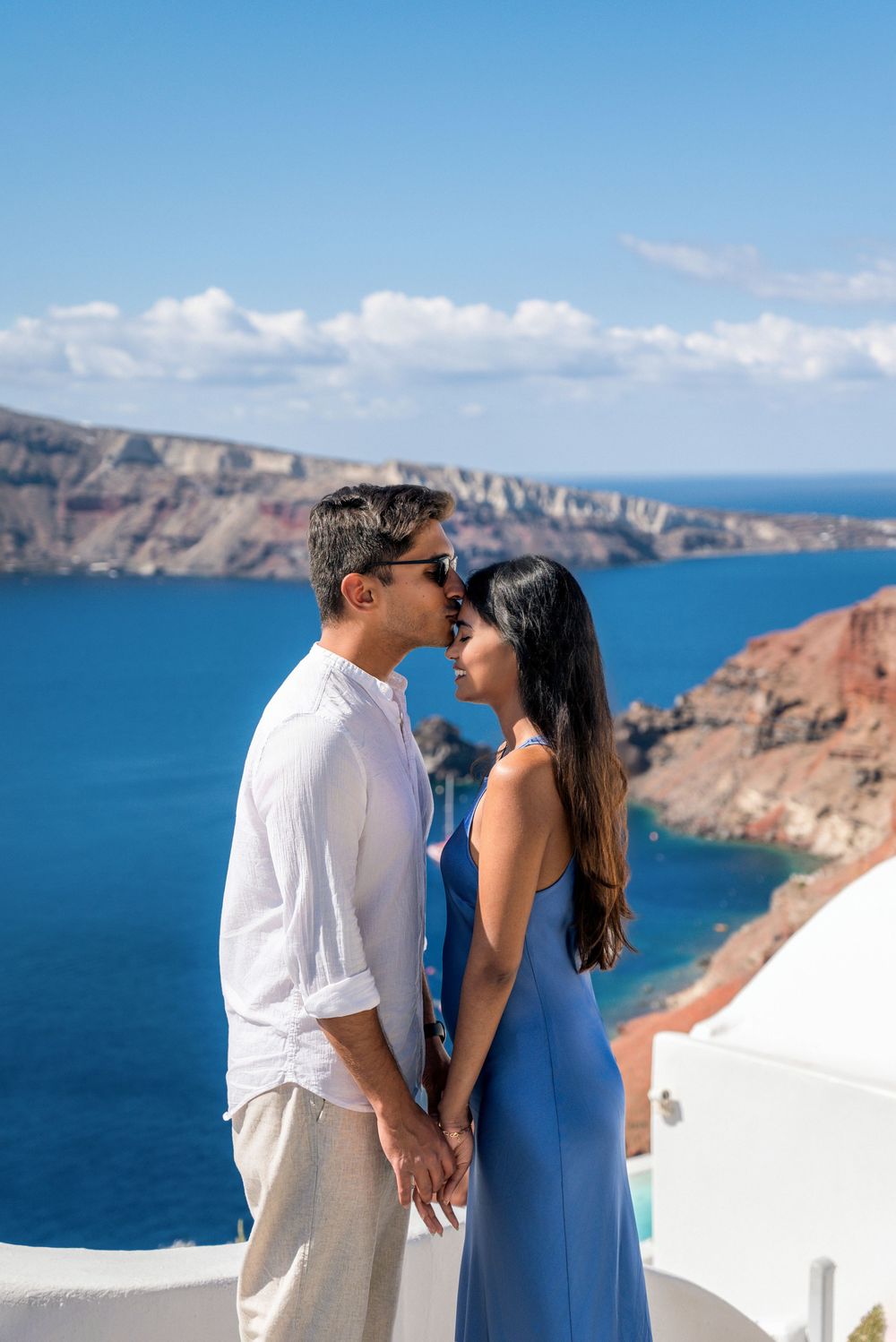 Romantic couple sharing intimate moments against stunning blue Mediterranean Sea views in Santorini, Greece.