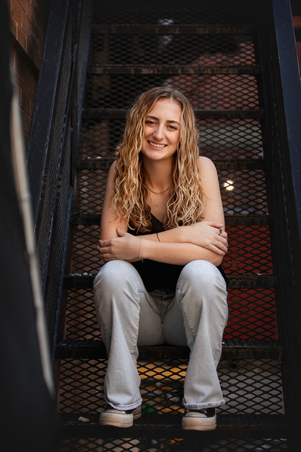 Senior graduate casual portrait sitting on metal stairs in relaxed pose.