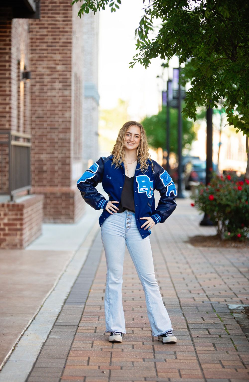 Senior graduate portrait Street style photo in blue jacket and light jeans on brick sidewalk.