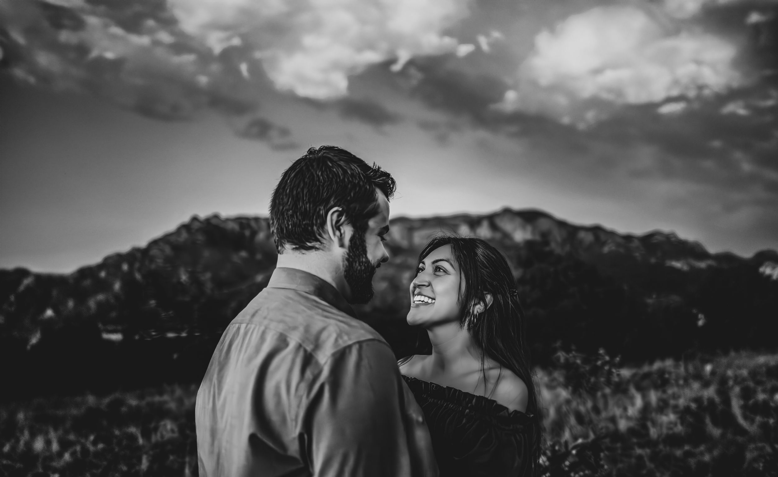 Black and white photo of couple sharing intimate moment with mountains in background.