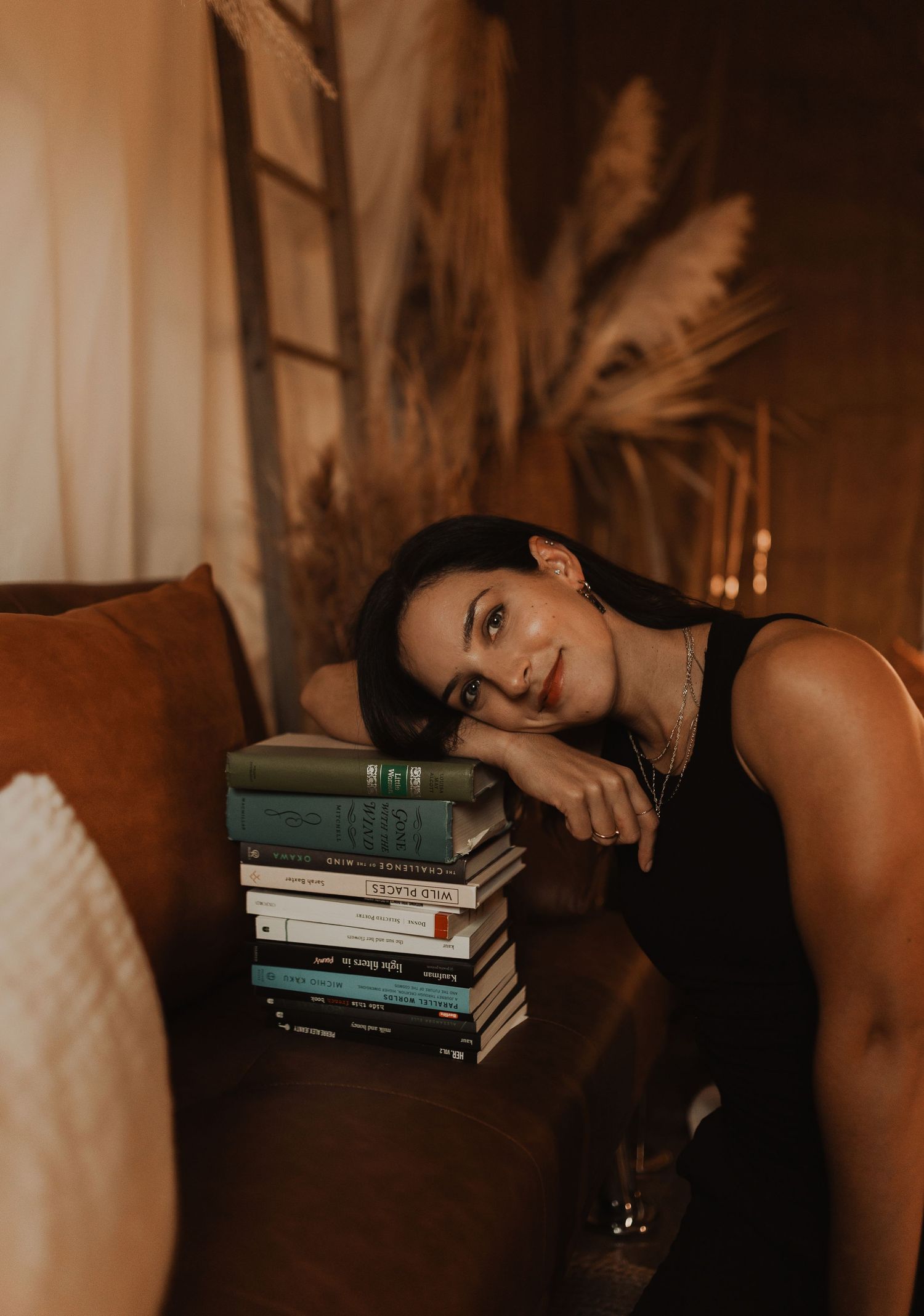 Contemporary bedroom scene with moody lighting features stacked books on white sheets in warm sepia tones.