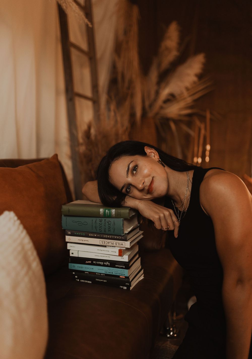 Contemporary bedroom scene with moody lighting features stacked books on white sheets in warm sepia tones.