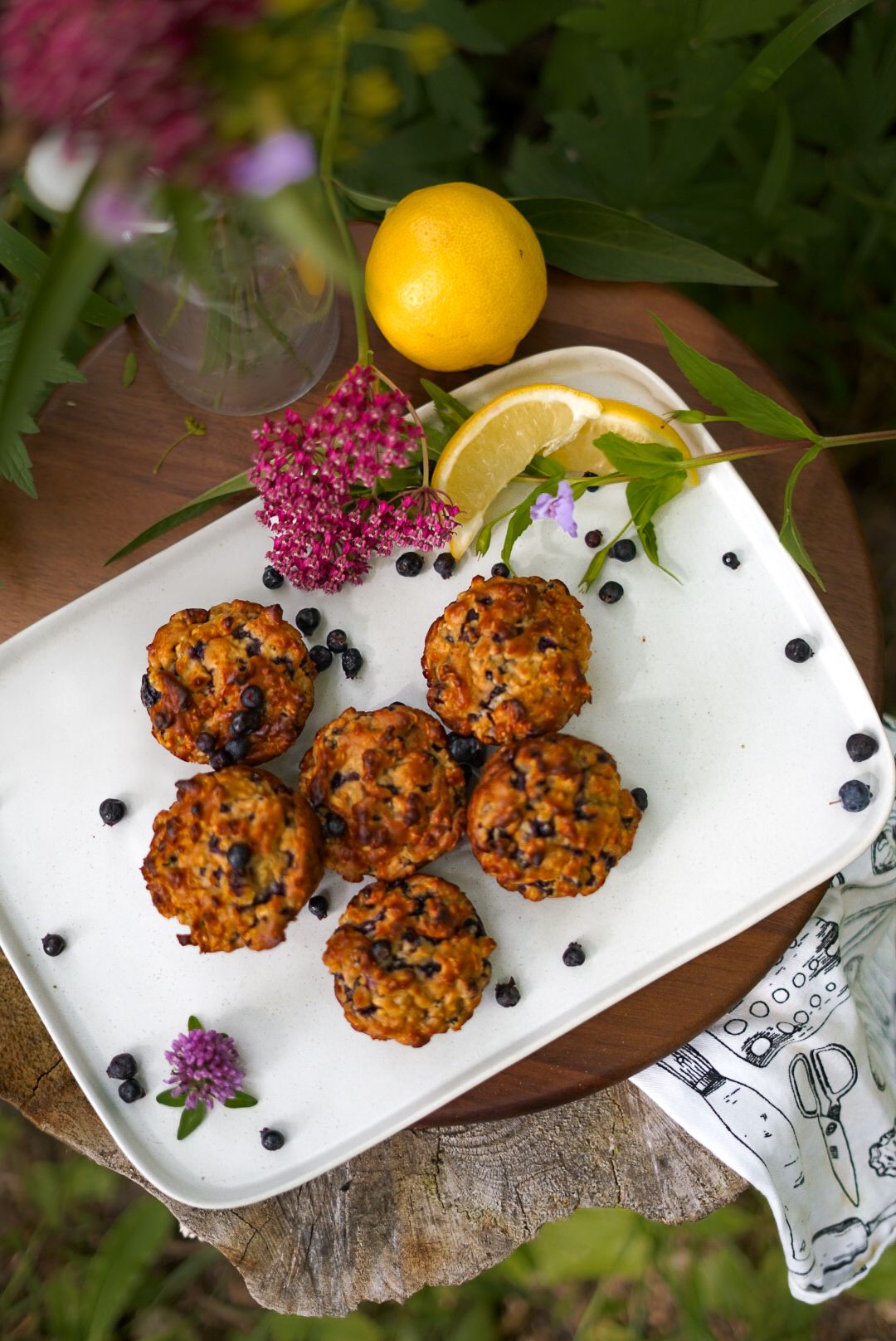 Homemade blueberry muffins on a white serving plate with citrus garnish and purple flowers.