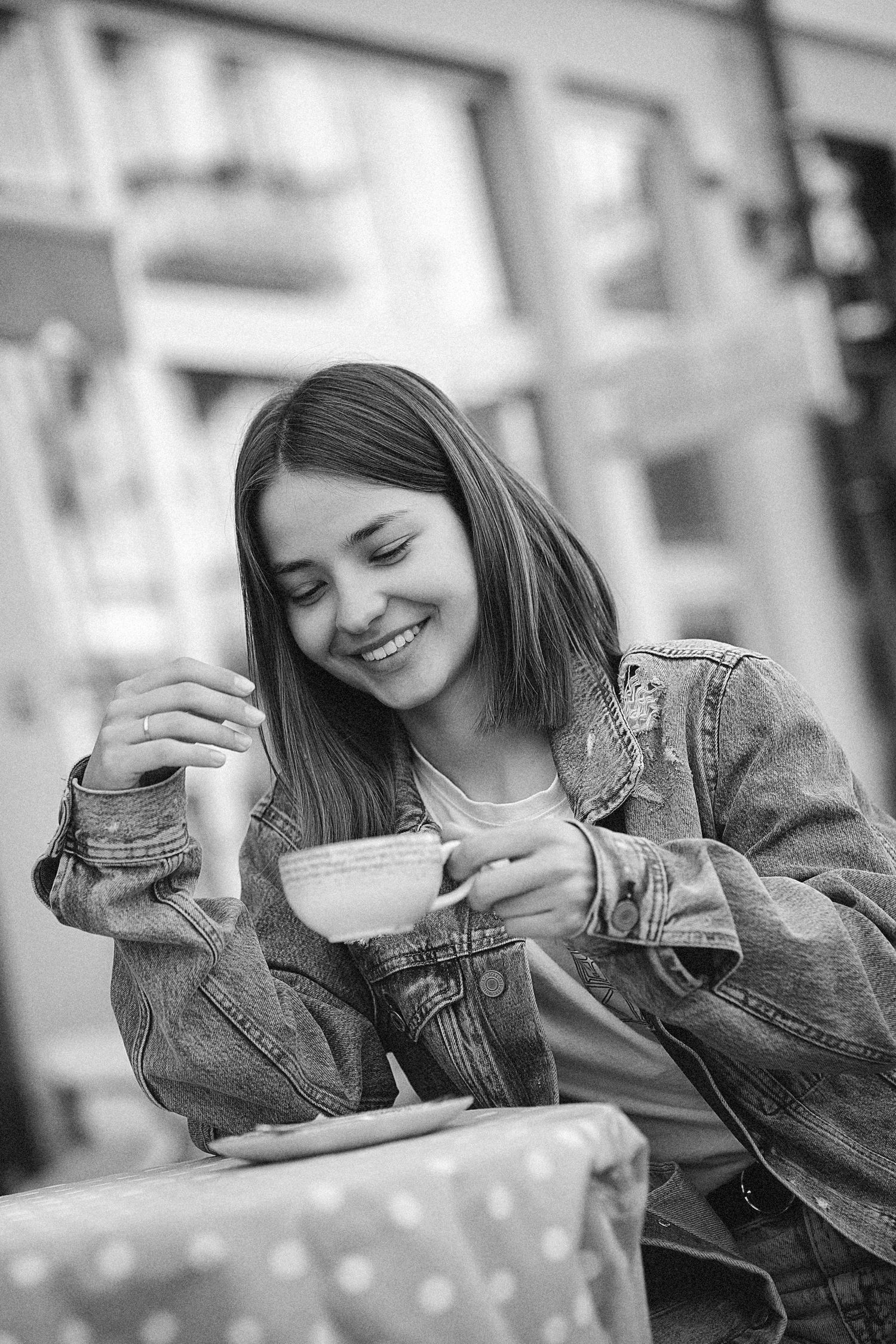 black and white portrait of a smiling girl  in a denim jacket with a bob haircut holding a cup of coffee