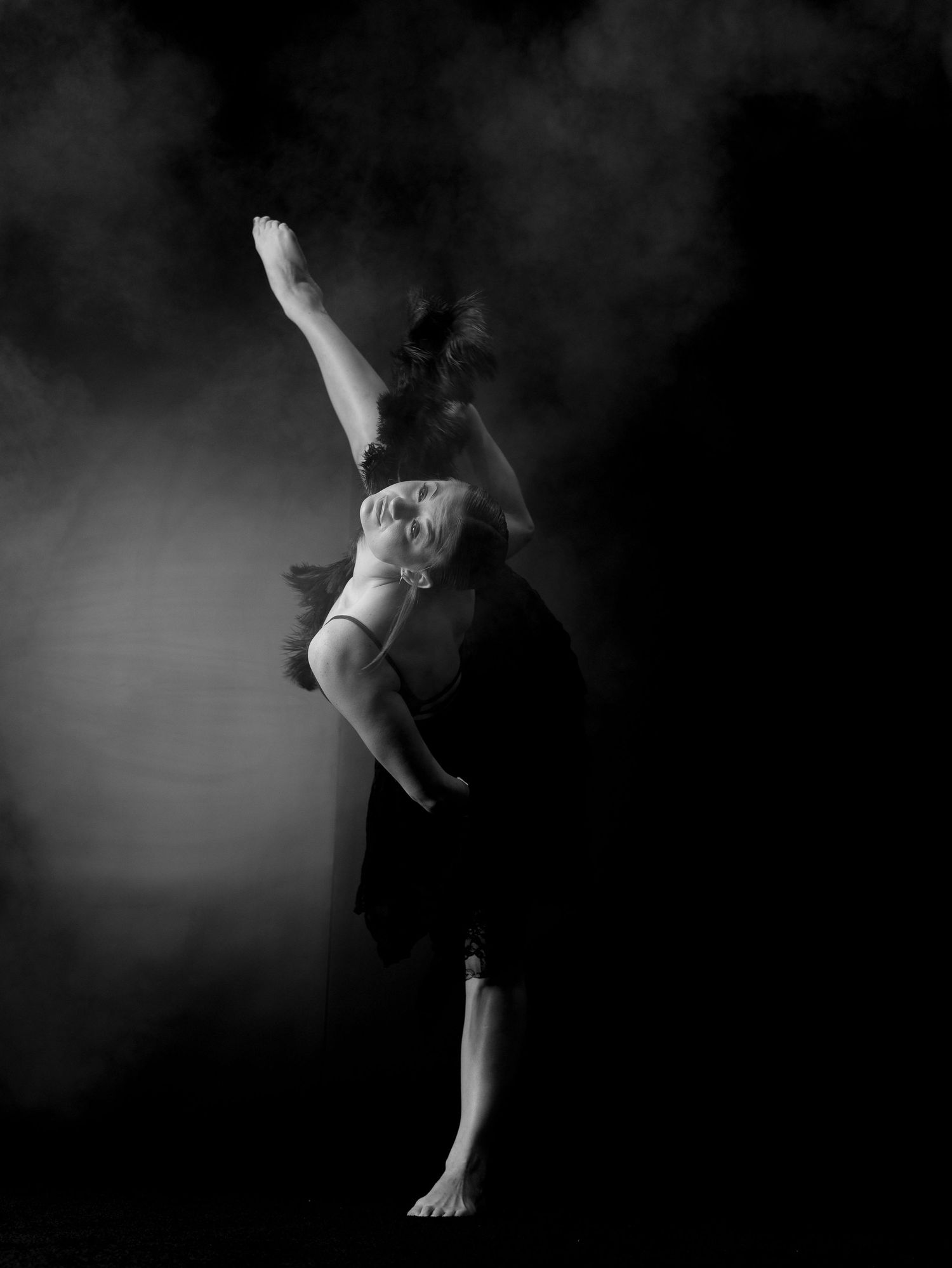 Black and white photo of a barefoot dancer leaping gracefully against a dark smoky background.