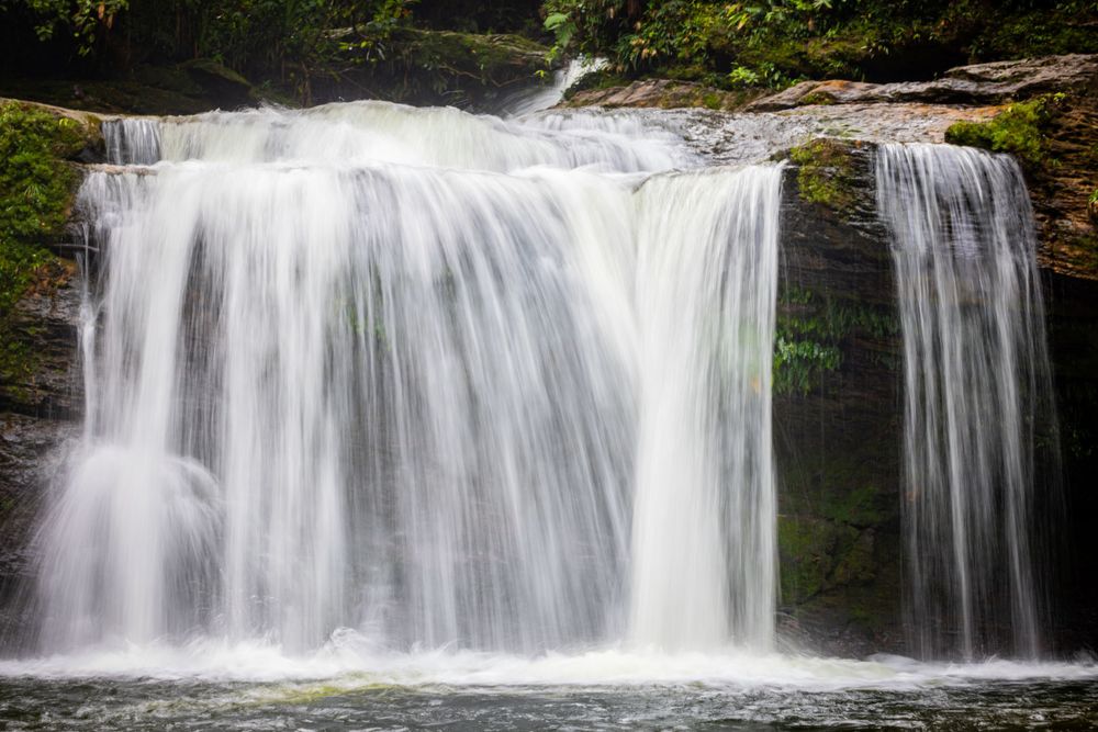 Wide cascading waterfall flowing over rocks in a forest setting.