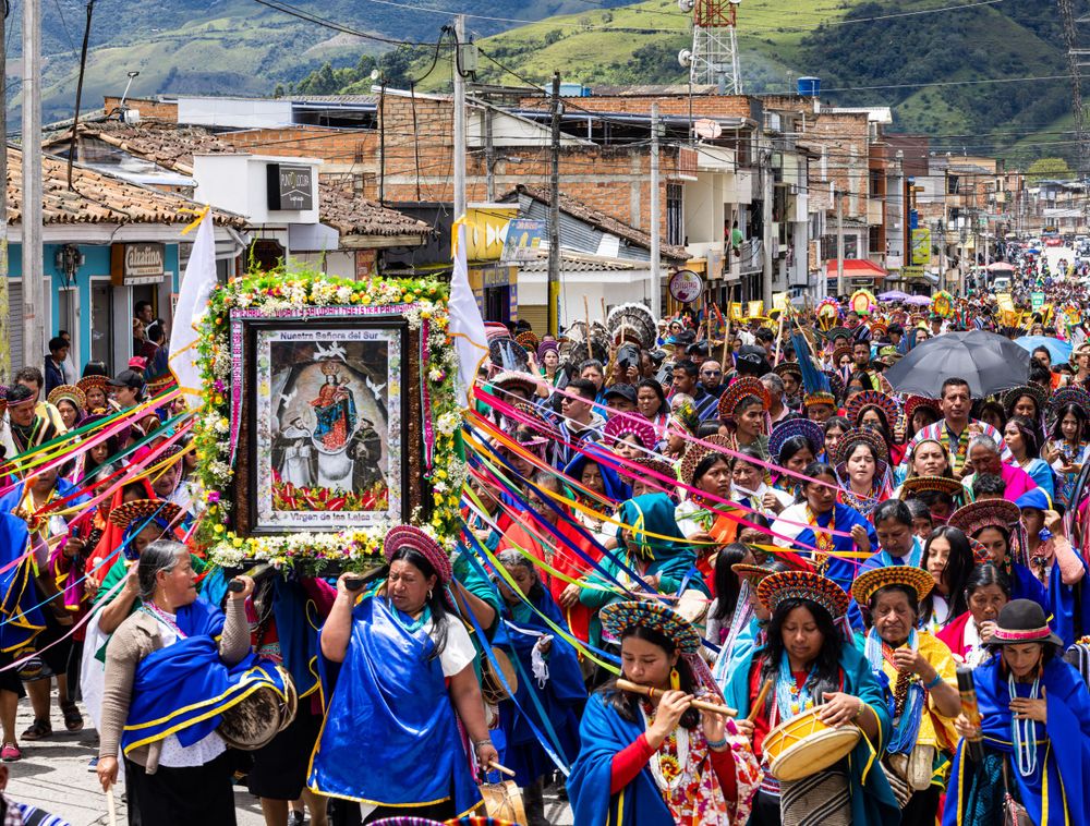 Colorful festival parade through city streets with crowds carrying banners and decorations.