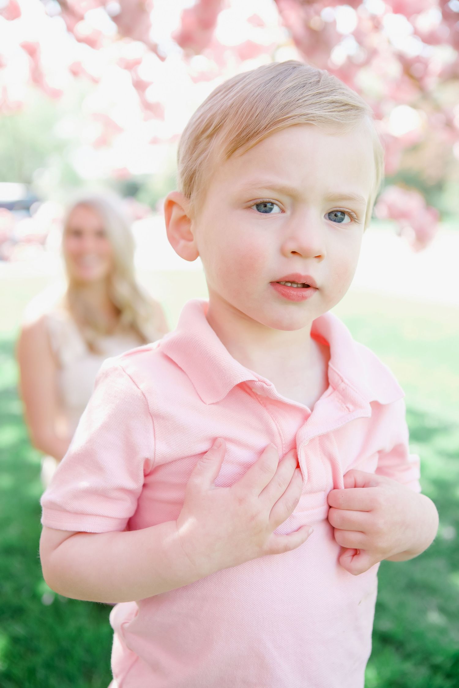 Child wearing soft pink clothing plays under spring blossoms.