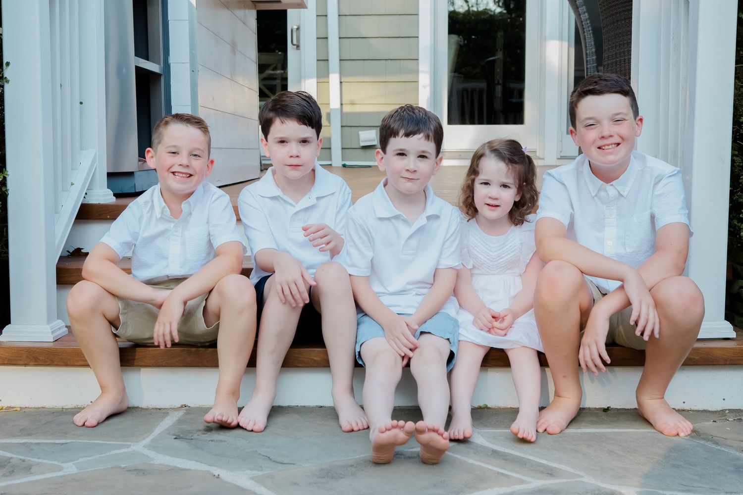 Group sitting on white porch steps wearing coordinated light colored outfits.