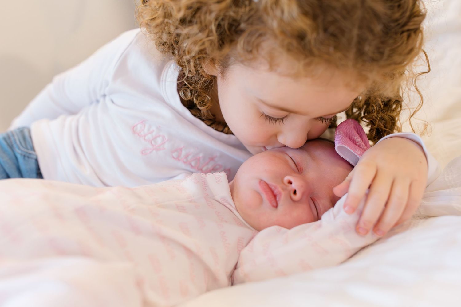 A sleeping toddler in a white bed with curly hair resting peacefully against white bedding.