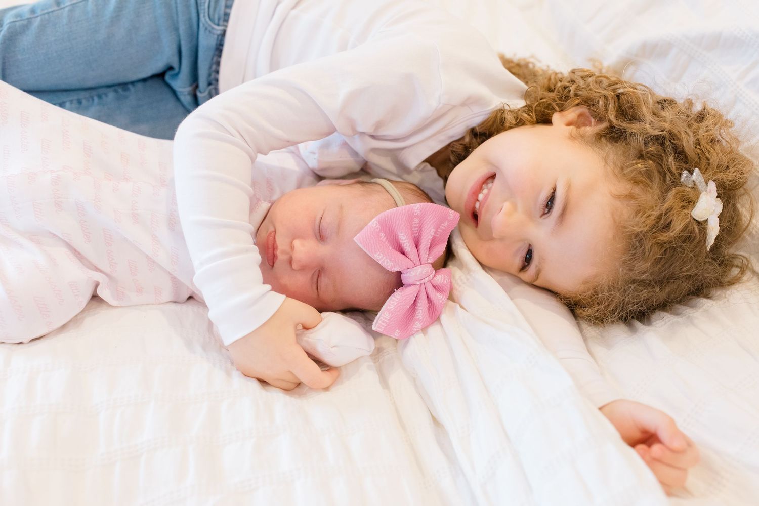 A sleeping figure with curly hair rests peacefully in white bedding while holding a pink bow.