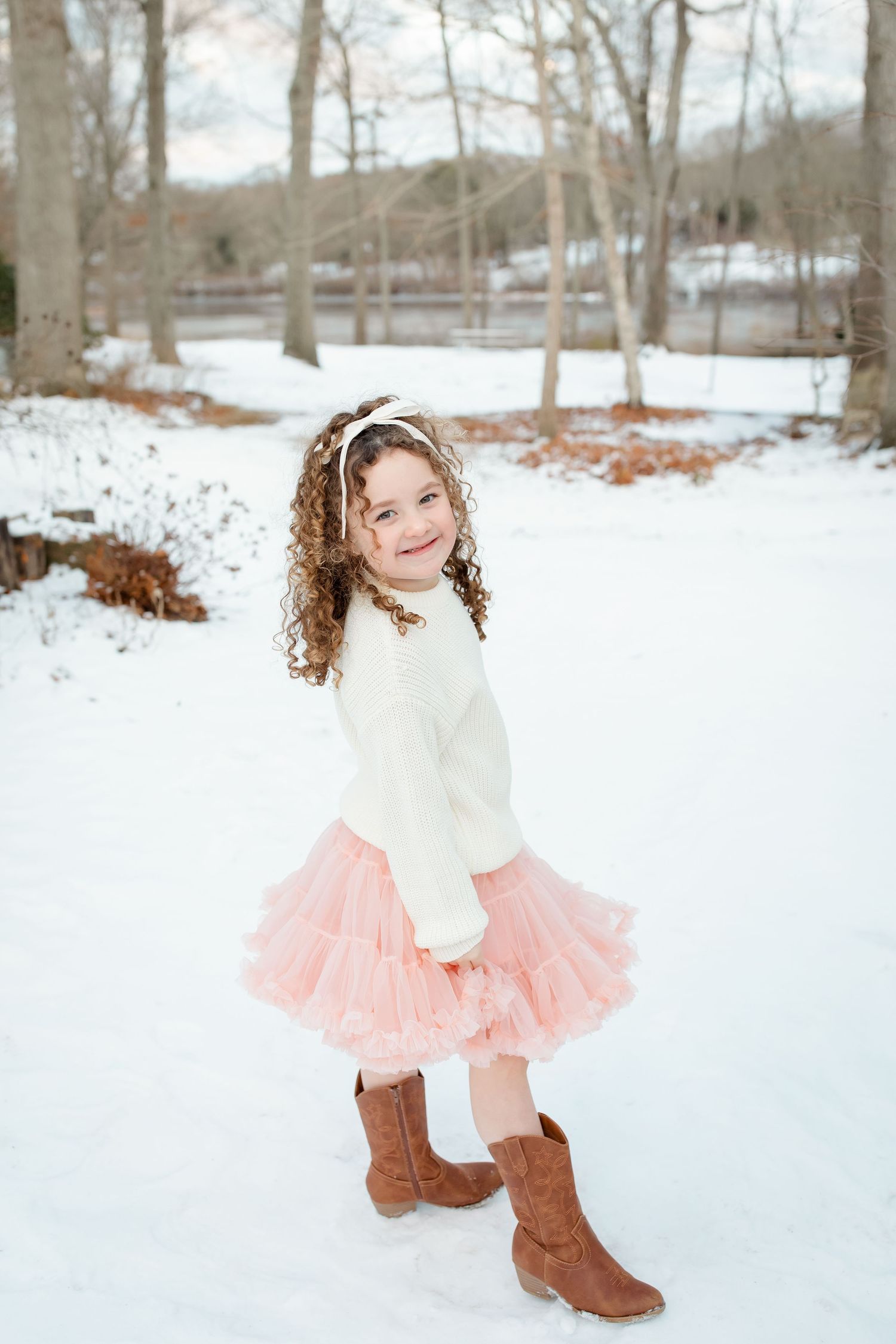 A series of winter portraits showing someone wearing a cream sweater and pink tutu skirt playing in the snowy landscape.