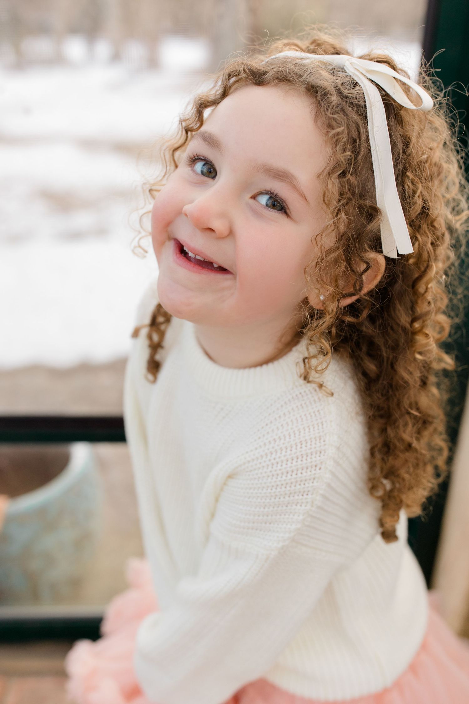 A child with curly hair and a white turtleneck sweater smiles and laughs joyfully in a series of candid portraits.