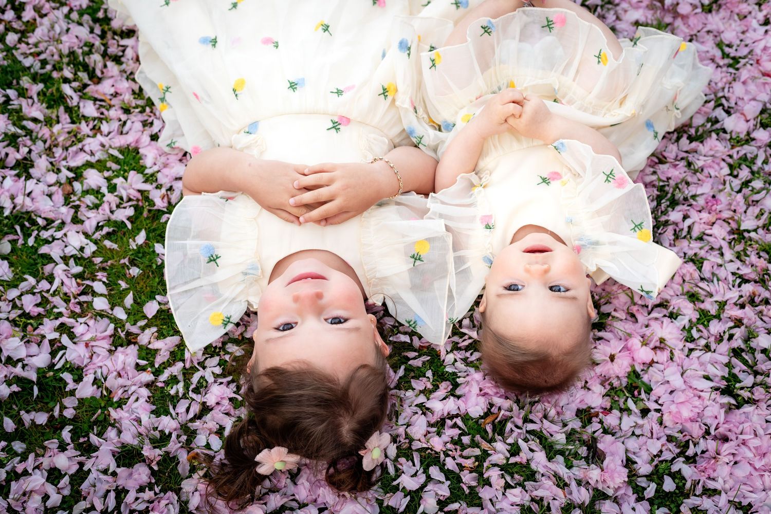 Two children lying on pink flower petals in white dresses creating a dreamy spring portrait.