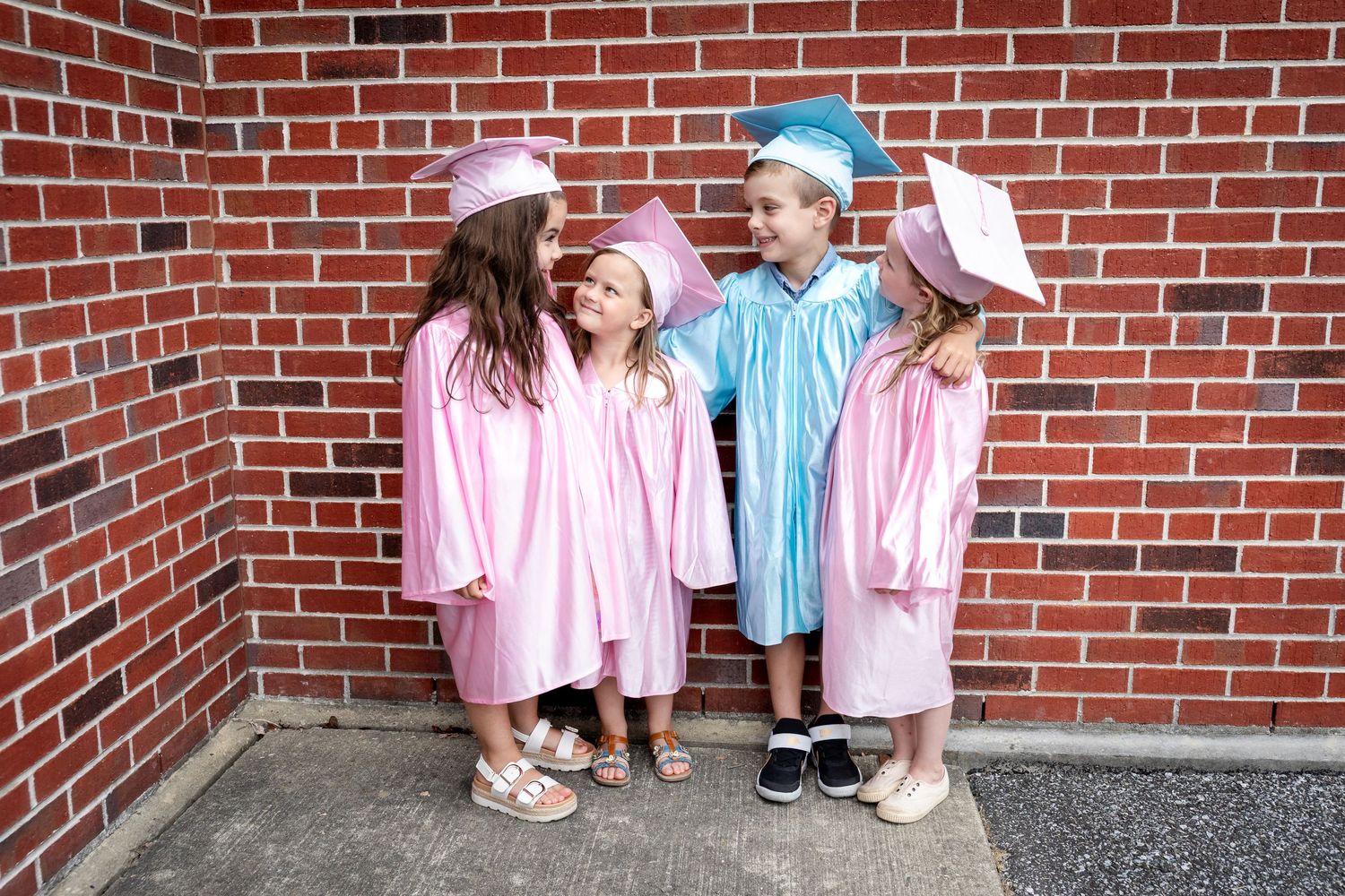 Three people in matching pink shirts and hats stand against a red brick wall.