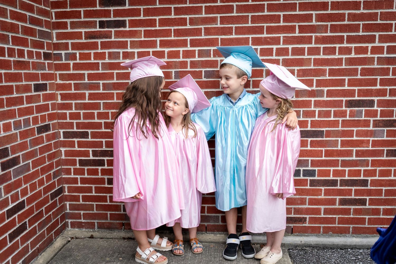 Children in pink and blue outfits pose against a red brick wall.