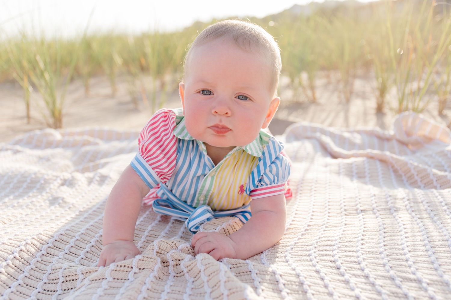 Baby lying on blanket during beach photoshoot with coastal scenery.