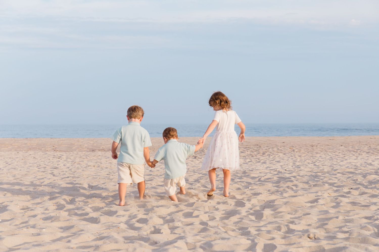 Family wearing white outfits walks together along a sandy beach at sunset.