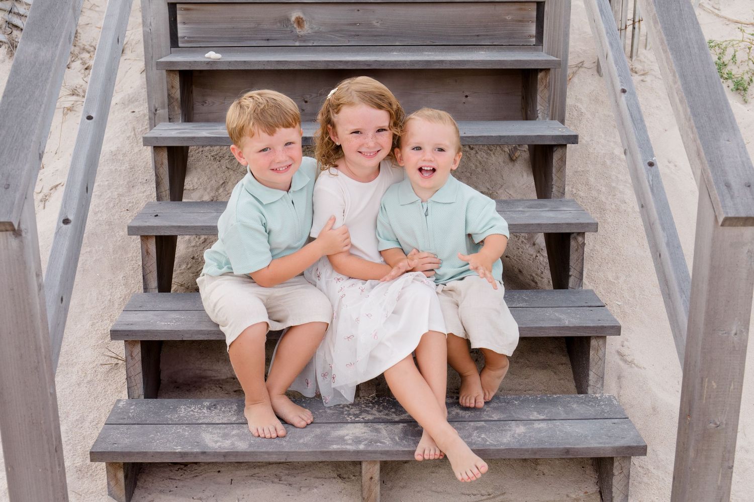 Family members pose casually on weathered wooden beach stairs.