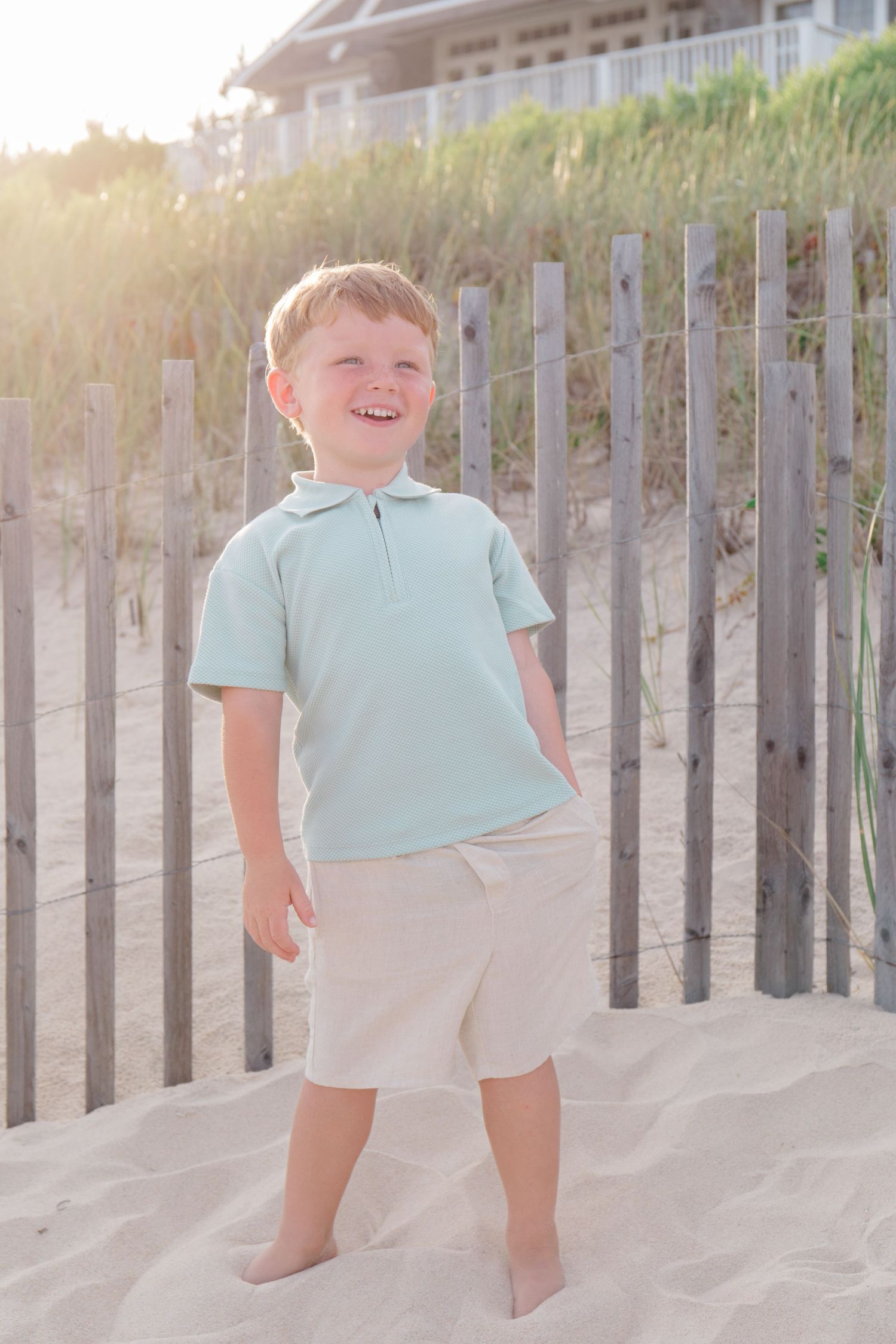 Children playing near beach fence posts during golden hour with beach house in background.