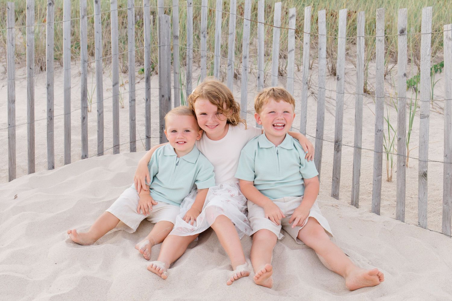 Beach portrait session with family members near wooden fence and sand dunes.