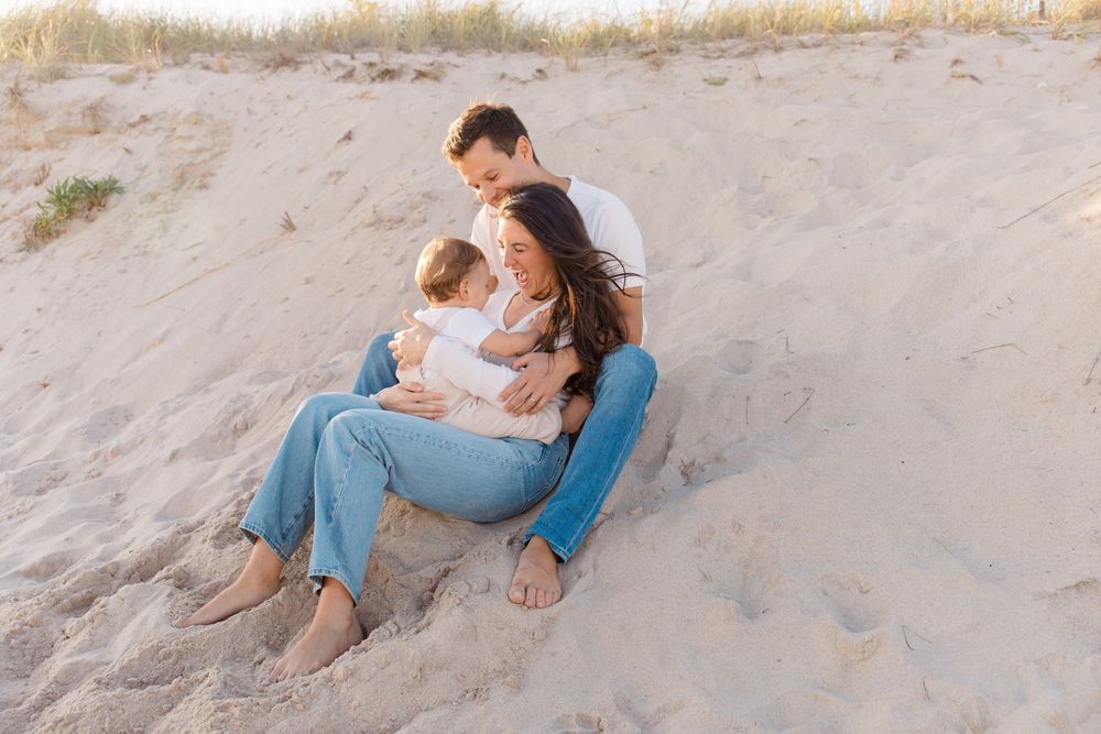 Family sitting together on sandy beach dunes at sunset by Hamptons photographer.