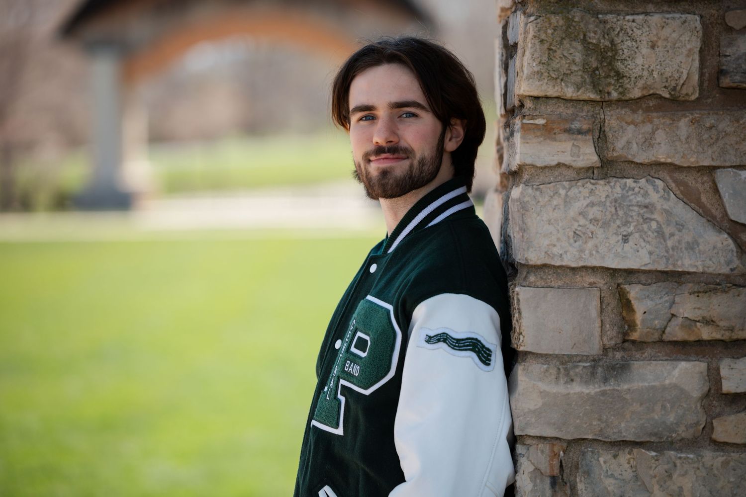 Green and white varsity jacket modeled against stone pillar and grass background.