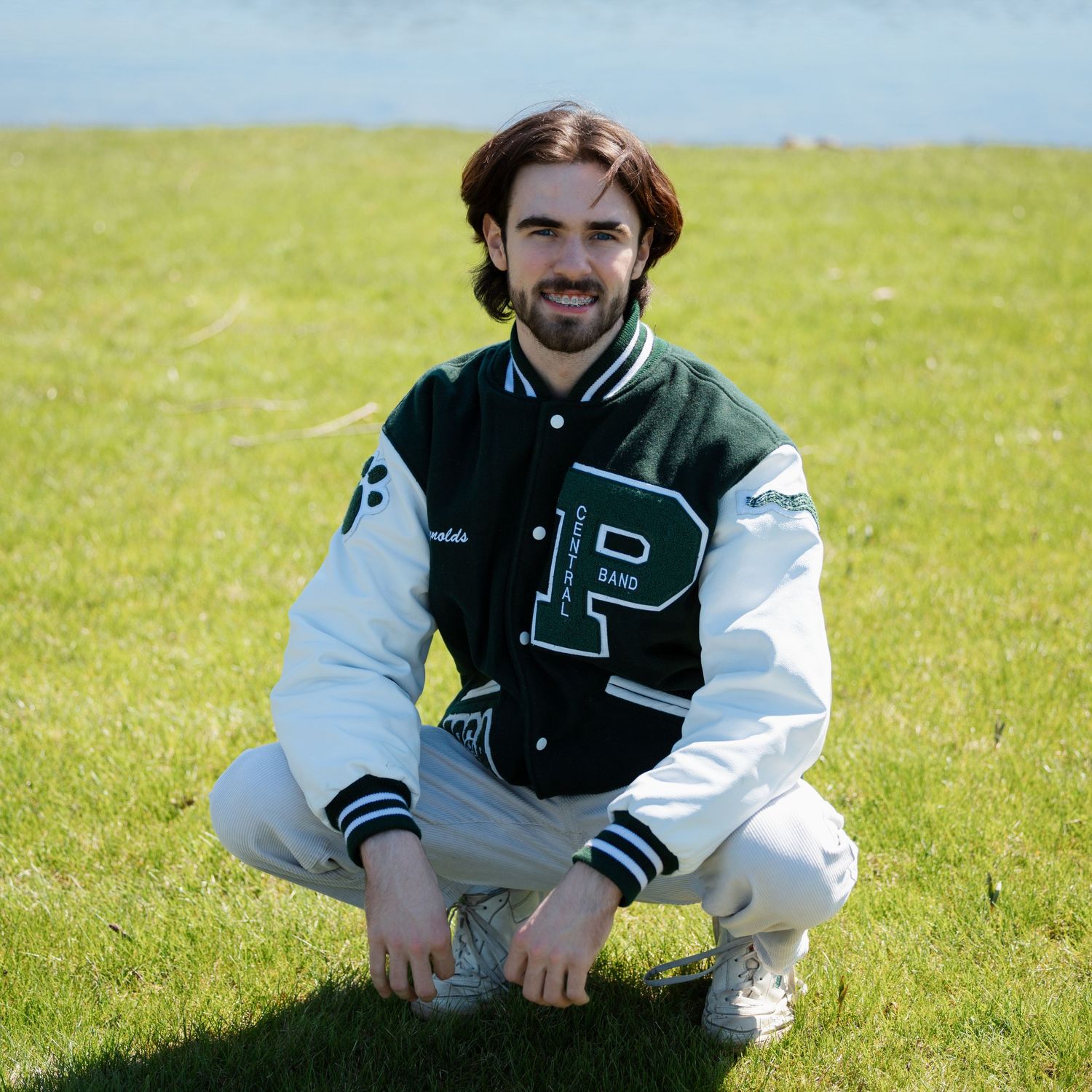 Athletic letterman jacket styled with white pants in sunny outdoor setting.