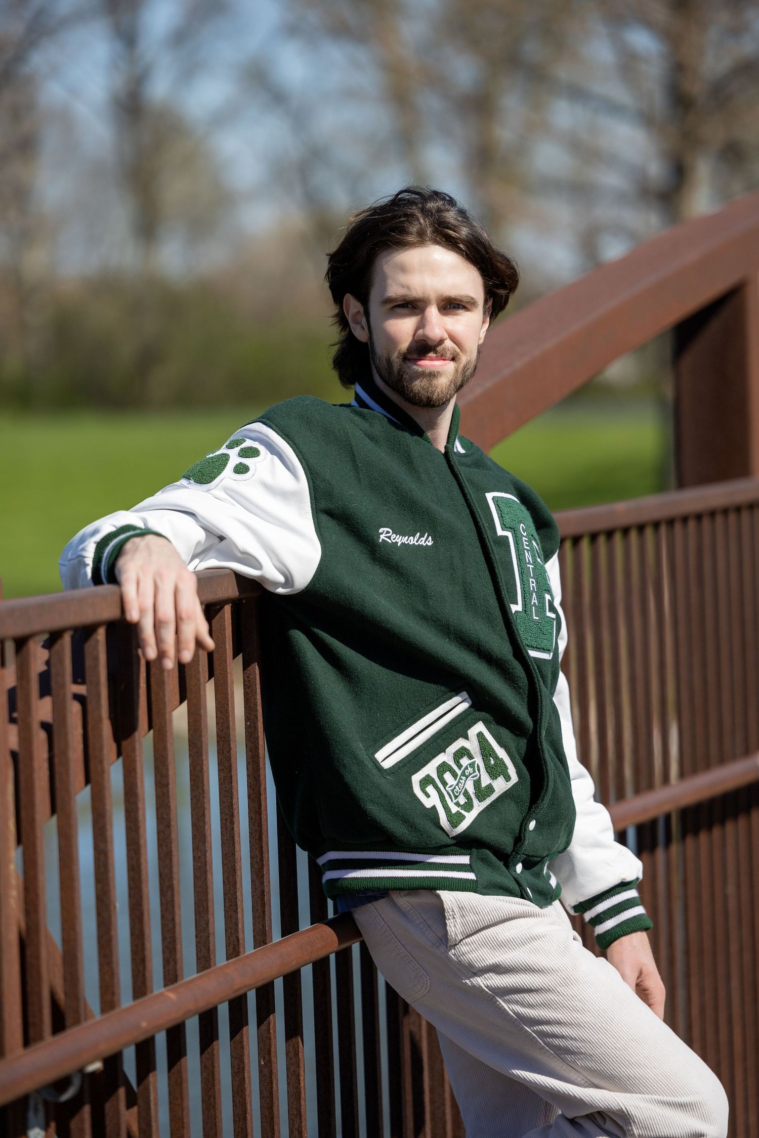 Vintage style varsity jacket modeled on wooden bridge in park setting.