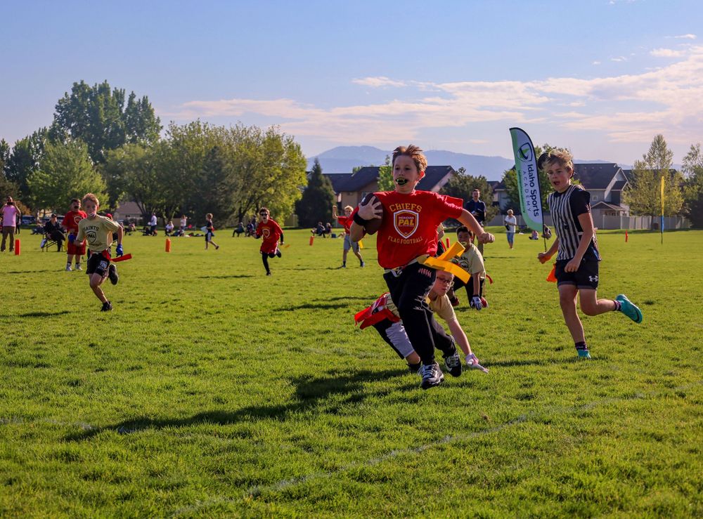 Players competing in an ultimate frisbee match on a grassy field with mountains visible in the background on a sunny day.