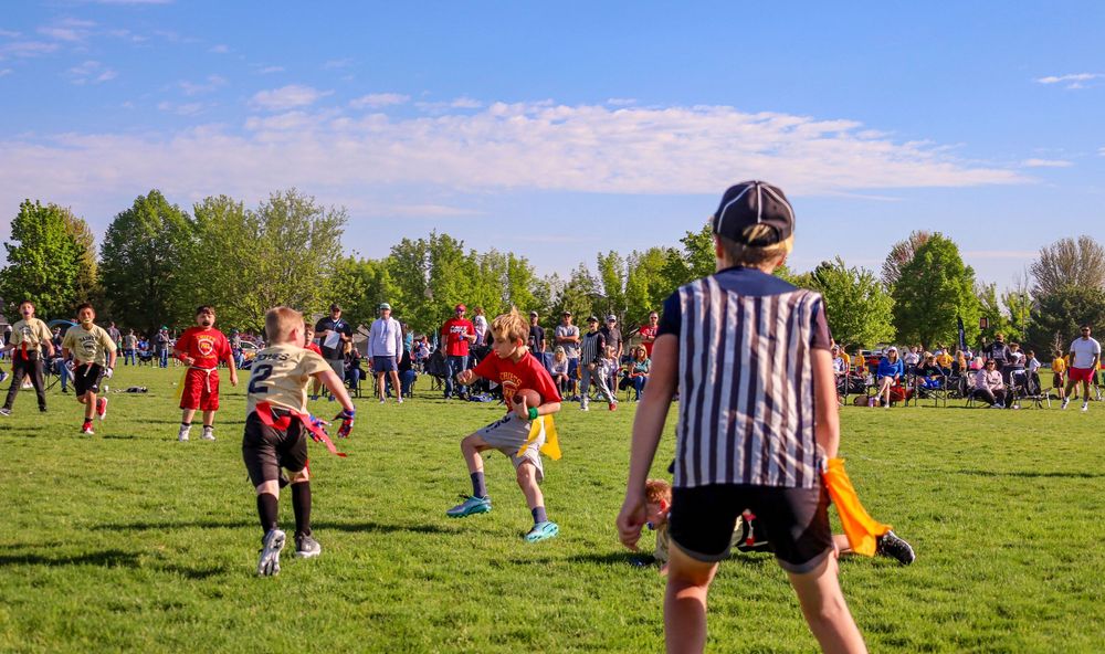 A group of runners gathers on a sunny green field with trees in the background during an outdoor sports event.