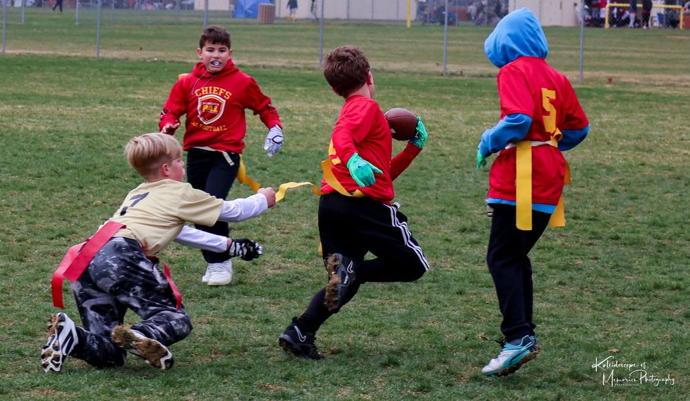 Kids playing flag football on a grassy field wearing red shirts and competing for flags during a match.