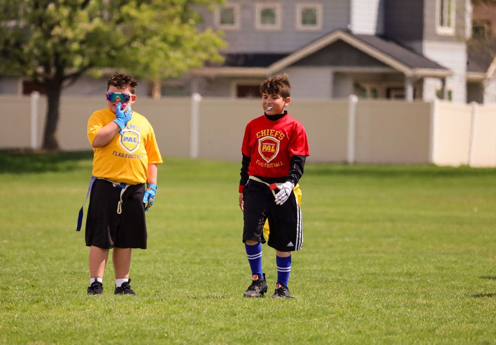 Two players stand on a grass field during a youth flag football game.