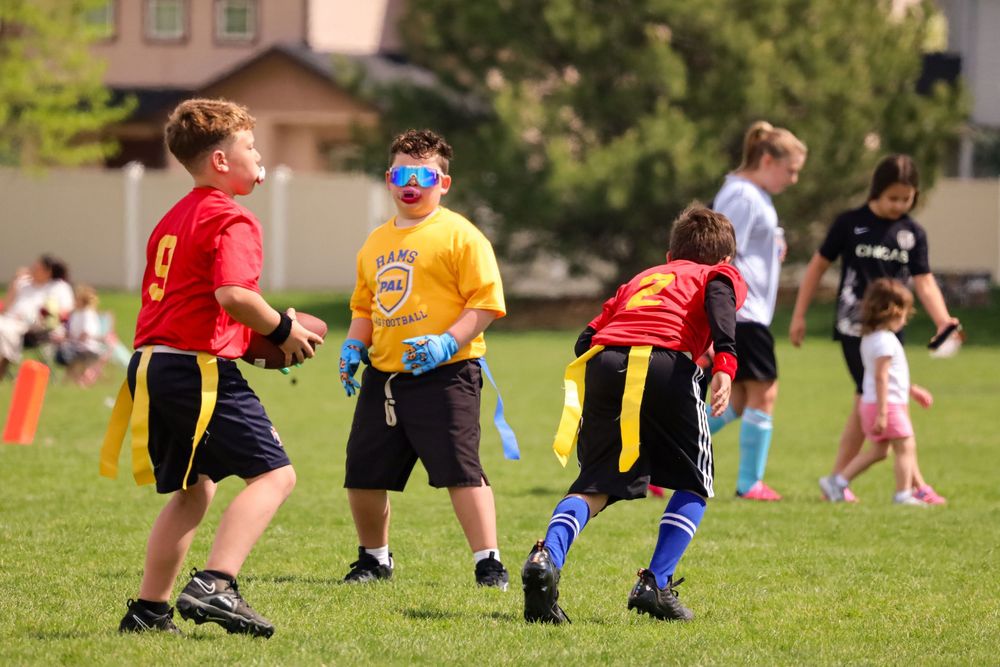 Elementary school kids playing flag football on a grassy field during a sunny day.