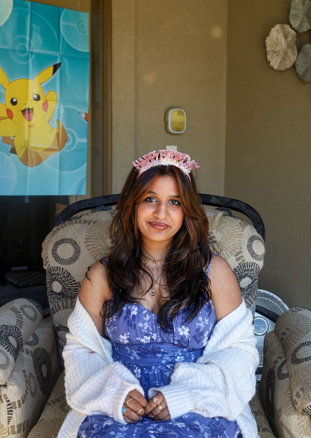 Someone in a blue dress and white cardigan sits in a patterned chair with a Pikachu poster visible on the wall.