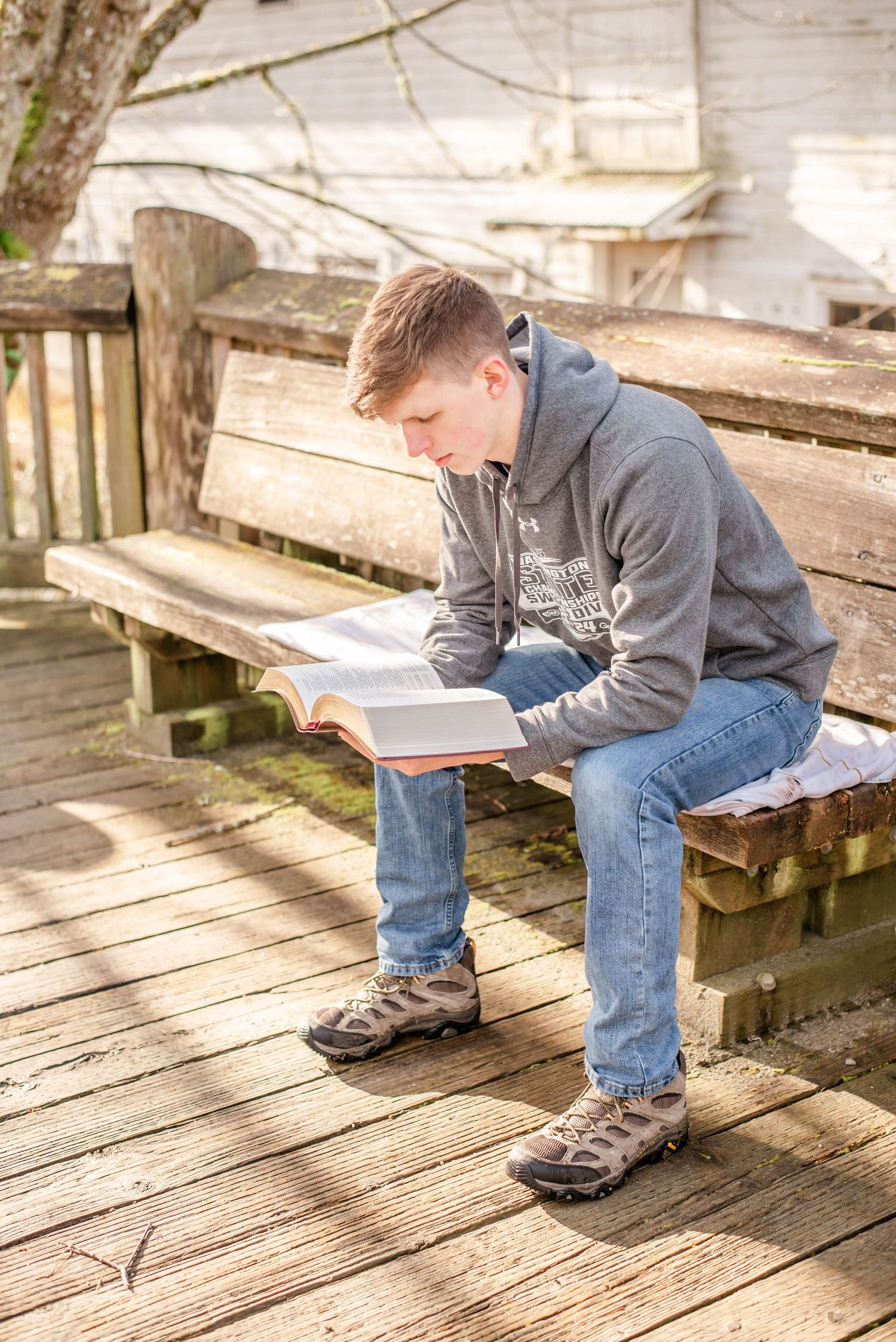 Person reading on weathered wooden deck steps in casual clothing.
