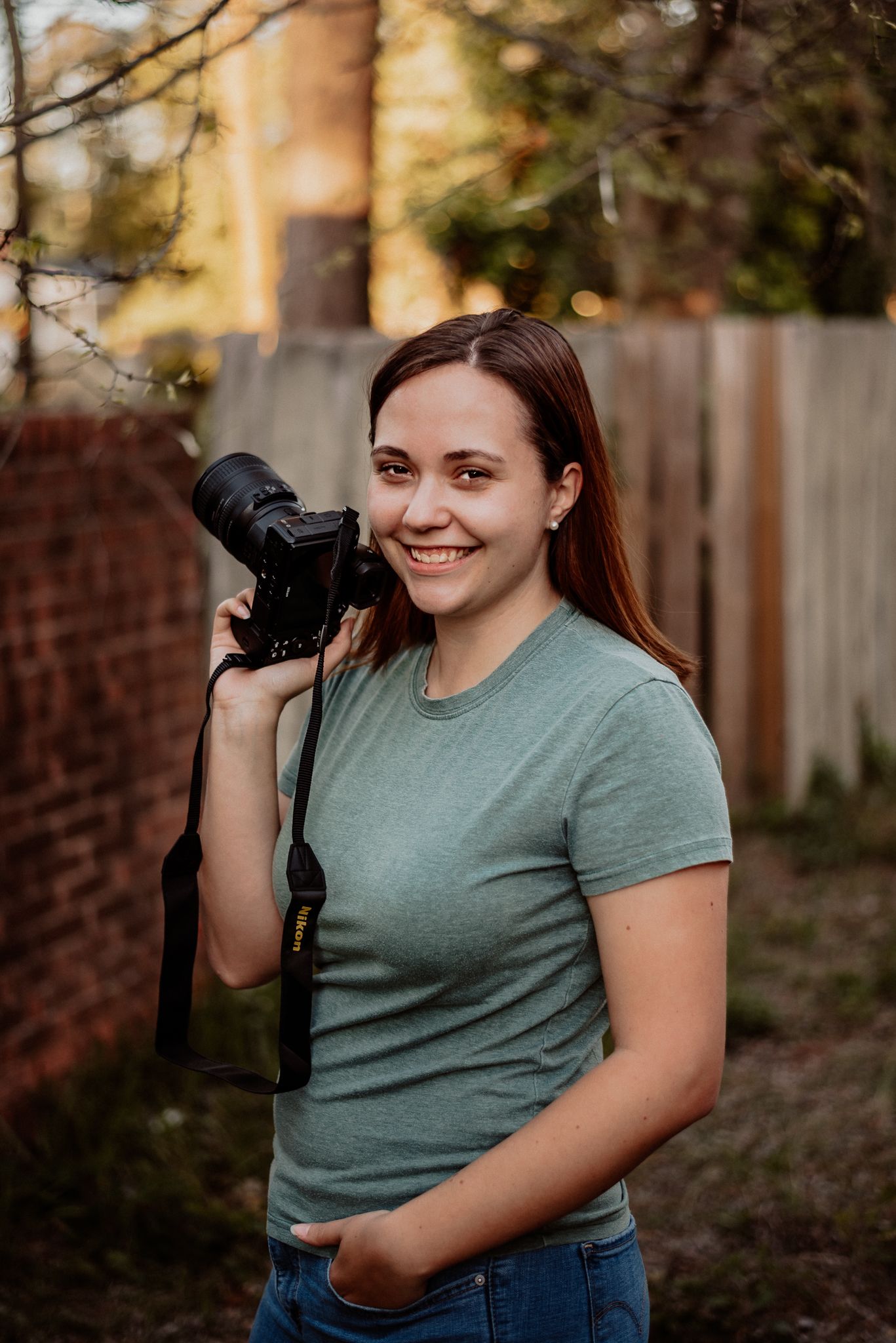 A photographer in a green t-shirt holds a professional camera outdoors.