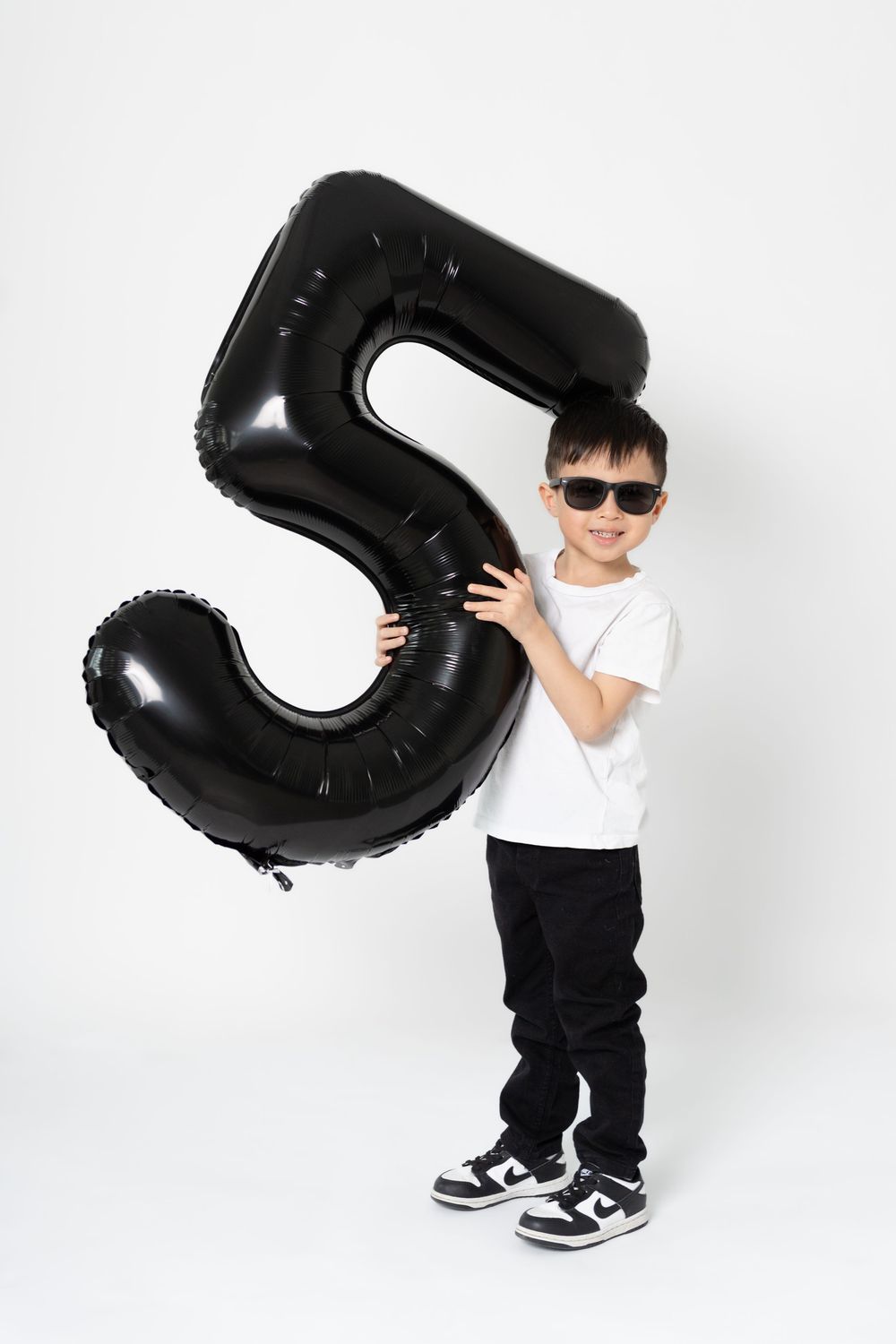 Three sequential photos showing someone holding and posing with a large black inflatable number 5 balloon against white background.