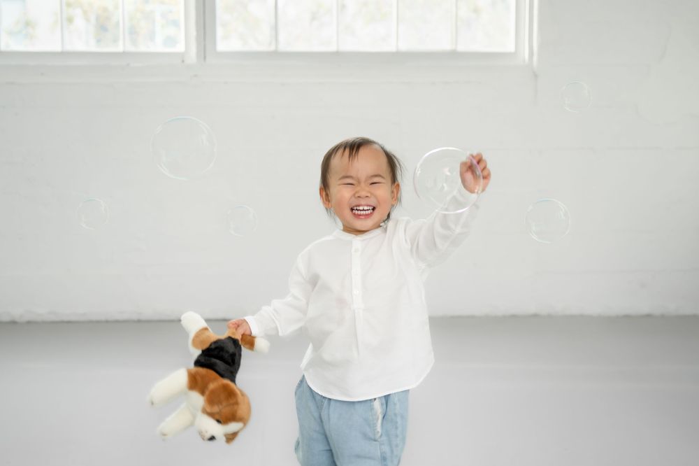 A series of five candid lifestyle photos showing a toddler in white clothing playing against a bright minimalist background.