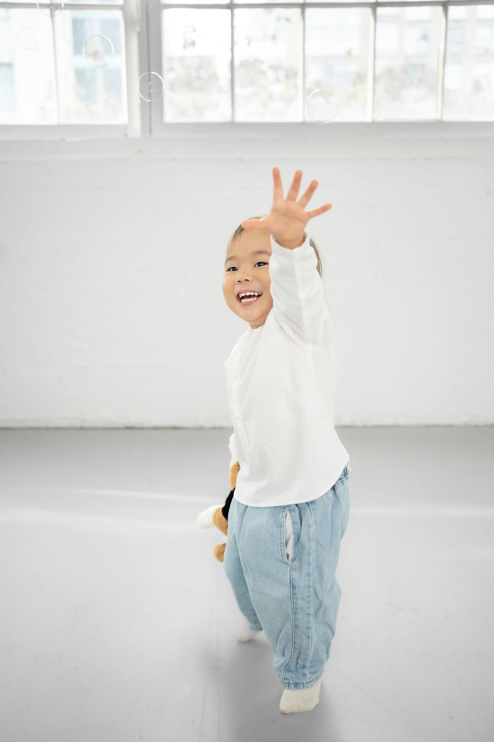 A sequence of four photos showing a child in a white sweater and light blue jeans waving and playing against a white backdrop.