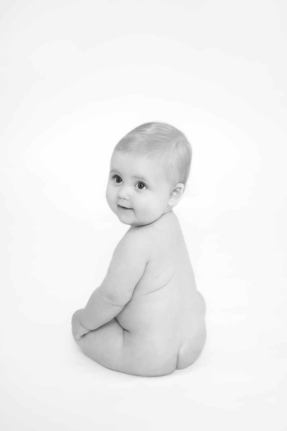 Three minimalist black and white photos of a baby sitting and turning, showing gentle curves and soft lighting.