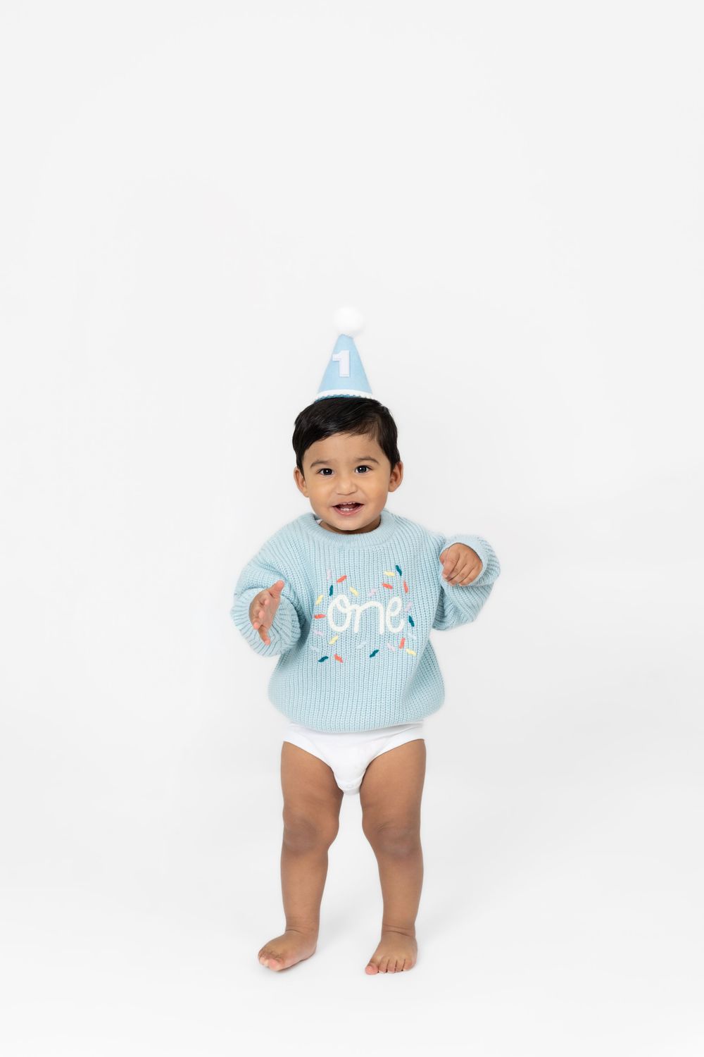A baby wearing a light blue knit sweater and white diaper poses against a white background.