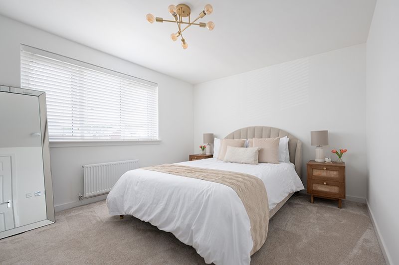 Bright white bedroom with beige upholstered headboard, window with horizontal blinds, and modern lighting fixtures.