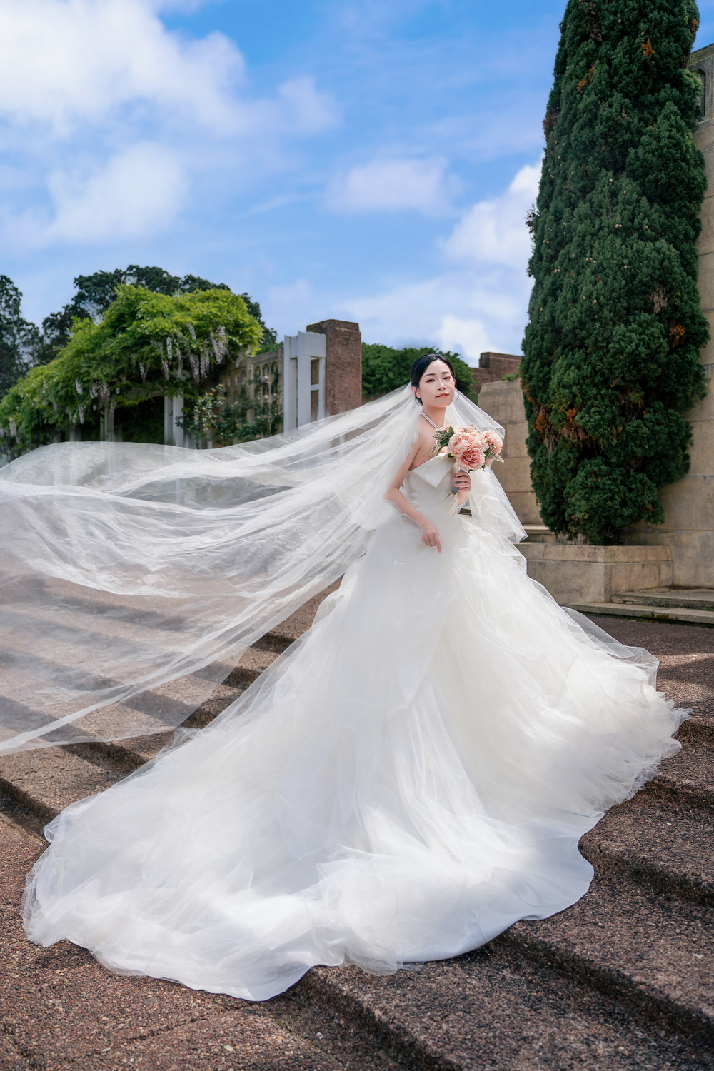 Beautiful bride with a long flowing veil and groom posing by historic stone architecture for Auckland wedding photography.